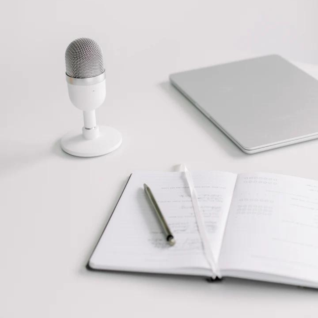 white microphone and notepad plus macbook on white tabletop