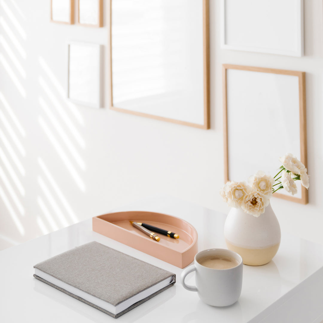 Bright room with coffee, vase, notepad, and pens on a desk and picture frames in the background