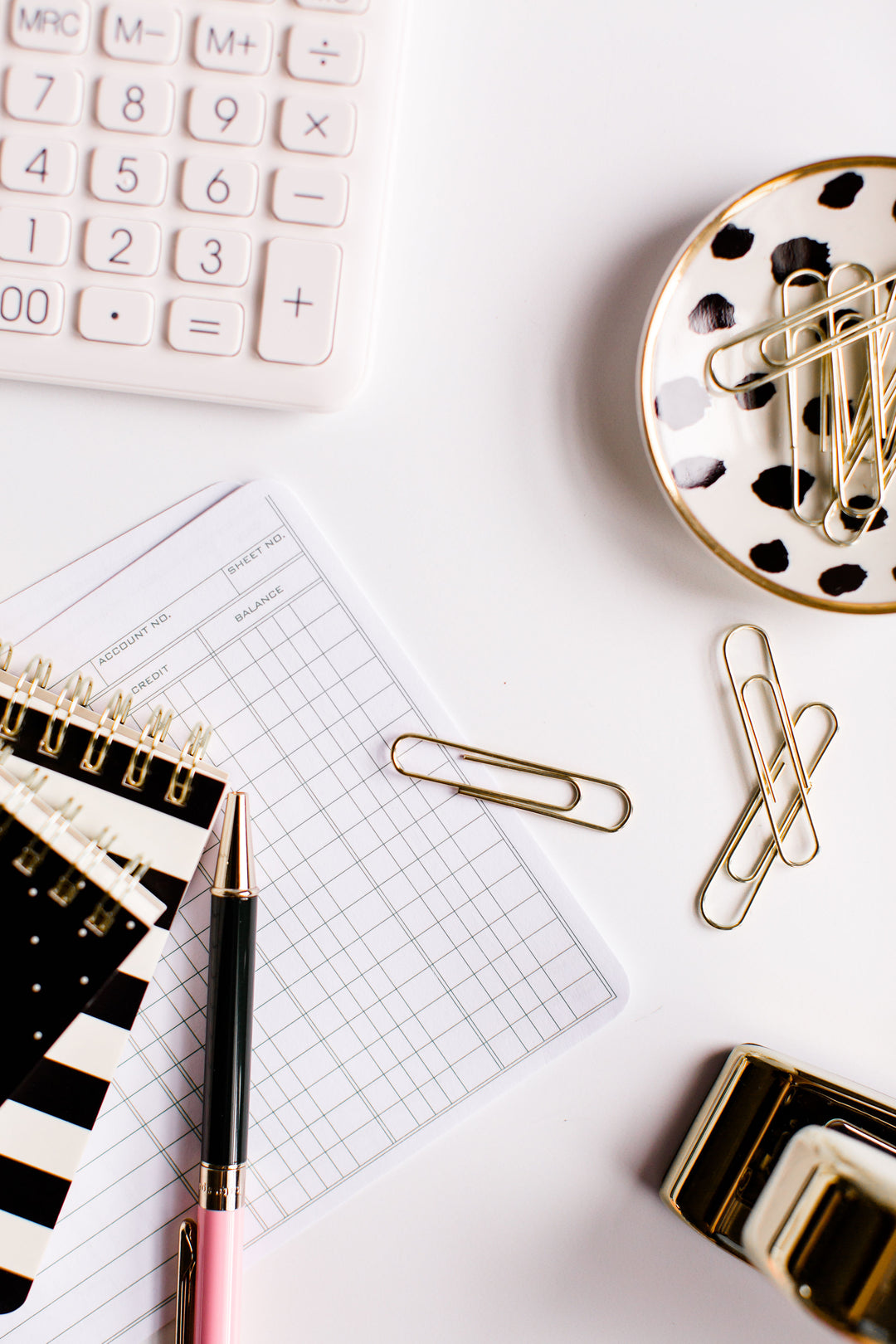 Top down shot of notepads, paperclips, calculator, and pen on a white desk