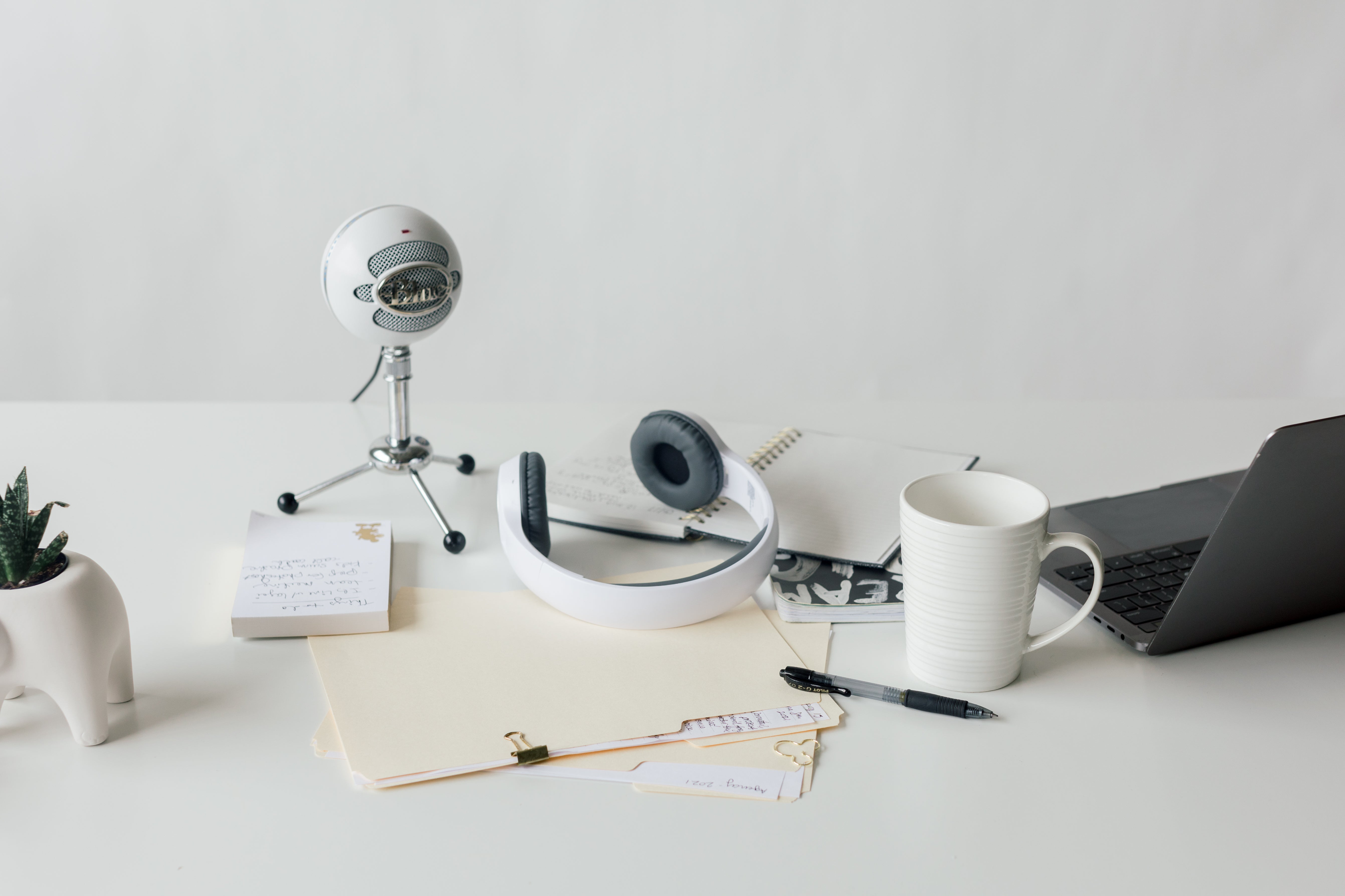 Rachel Brenke desk with retro microphone, headphones, files, pen, laptop, plant, and notepad.