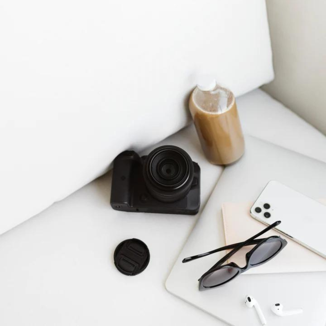 professional photo camera, lens, phone, airpods and cold brew sitting on a couch