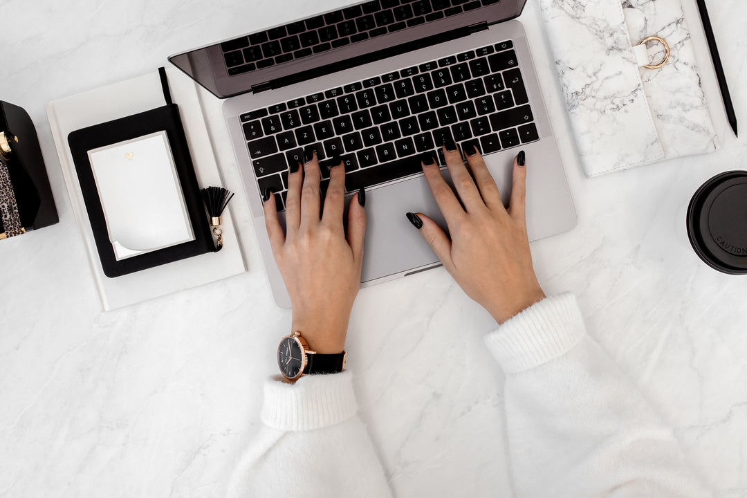 Lady with black nails typing on macbook top view of hands only