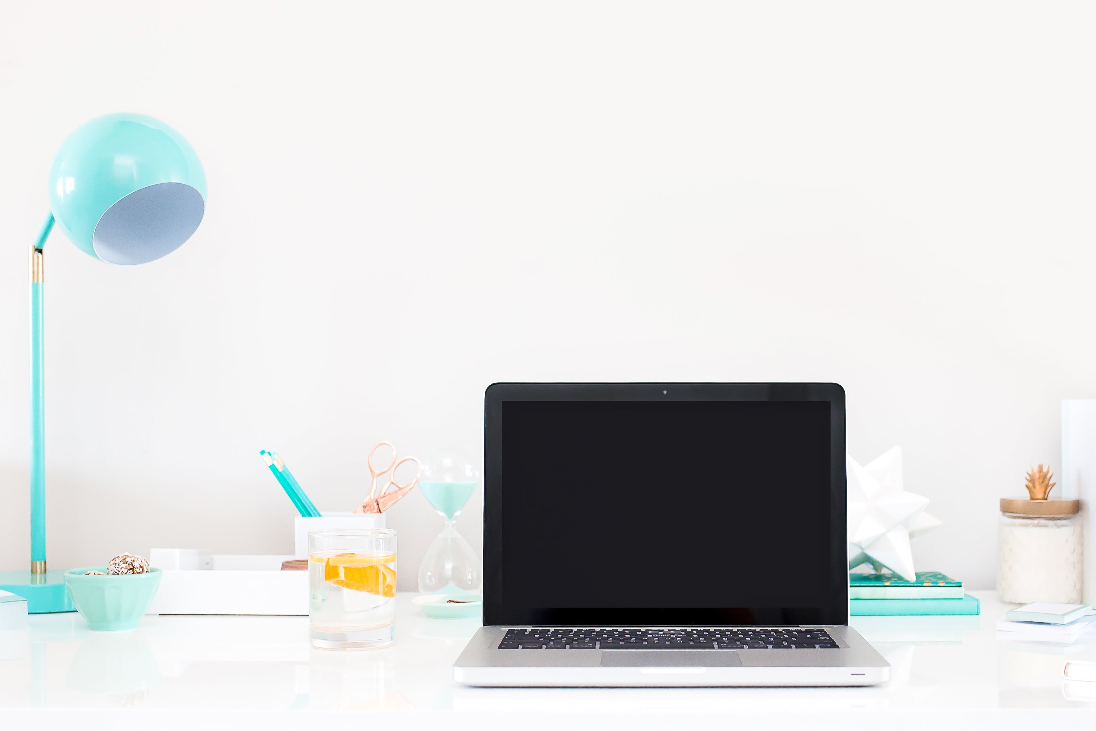 laptop on bright white desktop with baby blue lamp, pens, scidssors and other desk items